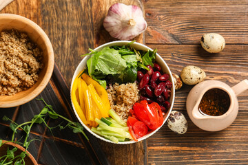 Healthy quinoa salad with vegetables in bowl and ingredients on wooden background, closeup