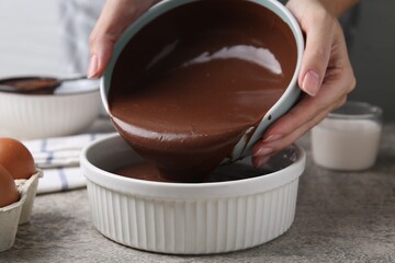Woman pouring raw chocolate dough into baking dish at grey table, closeup