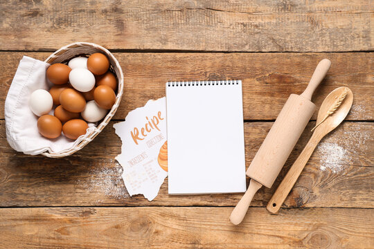 Blank recipe book with kitchen utensils, eggs and flour on wooden background