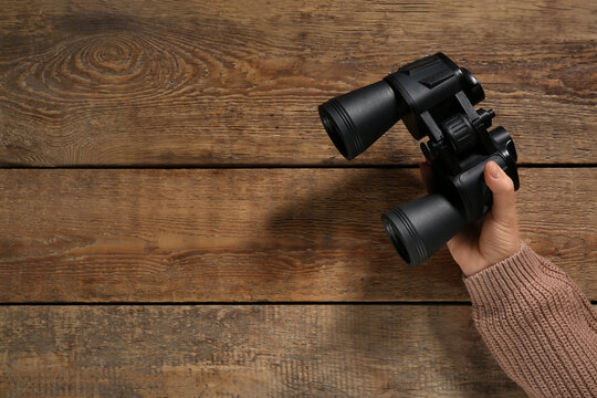 Female hand holding modern binoculars on wooden background