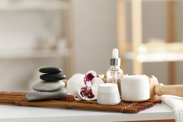 Bamboo mat with spa stones, massage roller and cosmetic products on table in salon