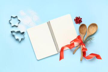 Blank recipe book with wooden spoons and Christmas cutters on blue background