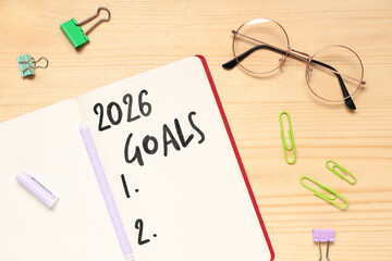 Notebook with 2026 goals, eyeglasses and paper clips on wooden background