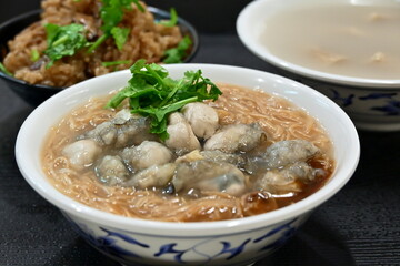 Bowl of traditional Taiwanese oyster vermicelli with tender red noodles, fresh oysters coated in sweet potato starch, thick broth, cilantro, garlic paste in authentic Taiwan street food.