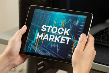 a male hands holding a tablet with the phrase stock market over a graph and chart concept
