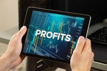 a male hands holding a tablet with the word profits over a stock market concept