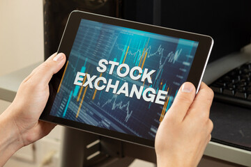 a male hangs holding a tablet with the phrase stock exchange over a graph and chart concept
