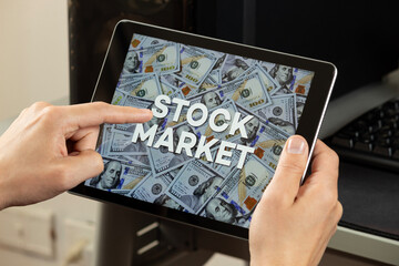 a male hands holding a tablet and pointing with his finger the phrase stock market over a dollar bills concept