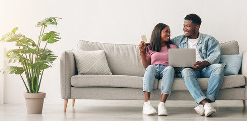 Online Payment. Black Spouses With Laptop And Credit Card Sitting On Couch In Living Room Paying Online Or Shopping In Internet, Young African American Couple Using Computer And E-Banking, Copy Space