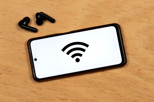 an a smartphone with the black wifi symbol over a white color and a wireless earphones over a cork background - Powered by Adobe