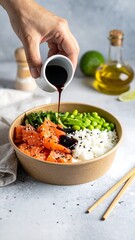 Hand pours sauce over a poke bowl