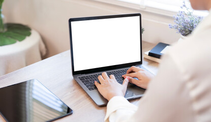 A person working on a laptop with a blank white screen, ideal for mockups, in a bright, modern office or home setting.