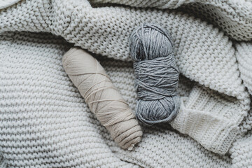 Knitting tools and various yarn balls are arranged on a soft, textured blanket, creating a warm,...