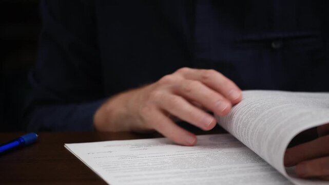 male professional hands carefully turning pages, stamping, and signing an important business document or legal agreement at wooden office desk, finalizing crucial transaction. close up.