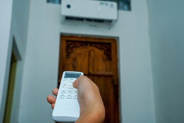view of a hand holding the AC remote control with the AC mounted on the wall.
