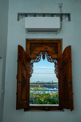 Wooden windows with carved motifs that open to reveal the outside view of water, trees and bright blue sky.