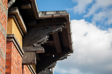 Ornate wooden dragon head carvings with striking red eyes adorn the roofline of a brick building against a blue sky. © DBA