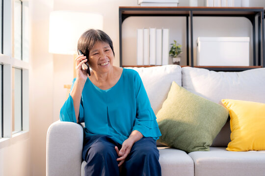 Senior asian woman telephone smiling and relax sitting on sofa in living room at home, cheerful elderly woman talking with smart phone sitting on couch in home, lifestyle and communication.