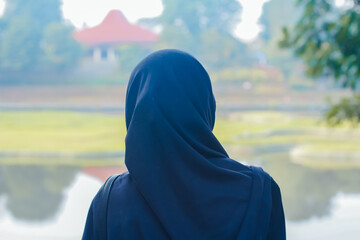 A woman wearing a blue hijab seen from behind while looking at a park landscape. Ideal for themes of contemplation, peace, and Islamic lifestyle