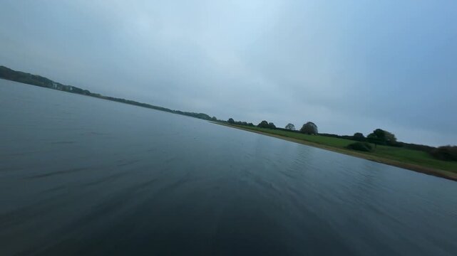 FPV drone aerial view close flying over wetland reserve with wild waterfowl birds and water control structures on reservoir late evening blue hour cloudy autumn night, United Kingdom 