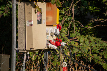 An outdoor electrical utility box with multiple power outlets and cables is mounted on a pole...