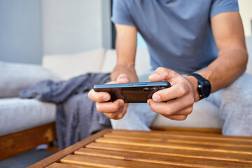 Man sitting on couch near house and using smartphone. Person relaxing and playing mobile games on terrace on summer day. Concept of digital lifestyle, leisure and gadget using