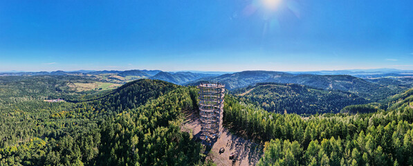 Aerial panoramic view of observation tower on forested mountain hill. Natural vast landscape with forest and distant ridges