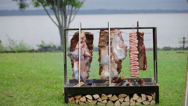 Wide shot of beef and sausages roasting on asado grill with Paran&aacute; River background in Corrientes, Argentina.