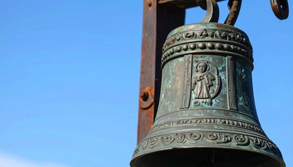 Fototapeta premium Ancient church bell with a relief of a saint and ornate decorations. Close-up detail against a blue sky, showing bronze texture and natural patina.