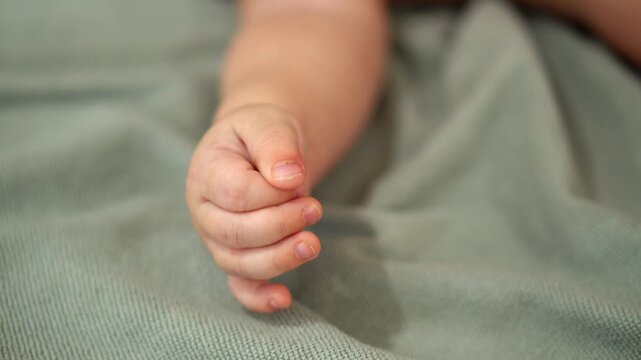 A baby's arm is on a bed. The baby's hand is curled up
