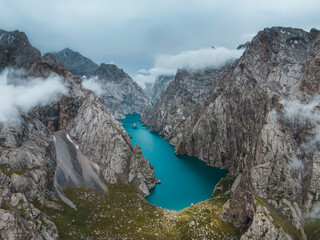 Aerial view of the deep blue Kol Suu Lake and its canyon, captured under heavy, dark clouds emphasizing the dramatic, rugged landscape