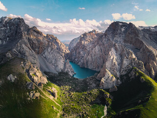 Wide aerial view of the turquoise Kol Suu Lake and its canyon, showing the surrounding green, rocky slopes and rugged, sunlit mountains