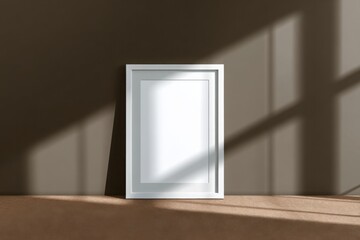 Vertical white frame leaning on a beige wall, surrounded by dramatic shadows and warm sunlight, ideal for artwork or poster mockup.