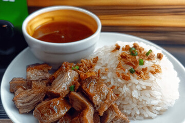 Hearty Filipino rice plate featuring seasoned meat and a rich dipping sauce, complemented by a light veggie side.