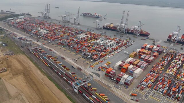 Aerial drone footage of busy international shipping port harbour with cargo containers, huge cranes for loading and unloading onto tankers ships, maritime economics, Port of London River Thames UK