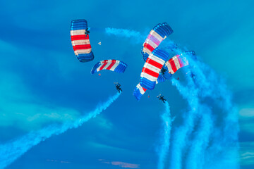 Colorful parachute team circles around the sky with smoke trailing behind them