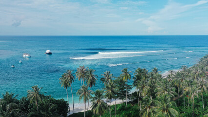 Aerial view of a tropical beach with palm trees, boats, and clear blue ocean water.