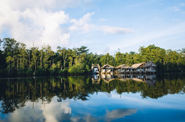 Fototapeta premium A serene waterscape reflecting buildings and lush trees under a cloudy sky.