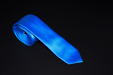 Rolled blue tie isolated on black background closeup view 