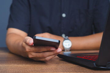 Businessman holding phone and working on laptop at desk.