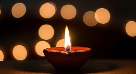 A single clay diya with a bright flame burning in the darkness.