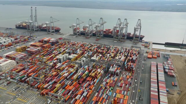 Aerial drone footage of busy international shipping port harbour with cargo containers, huge cranes for loading and unloading onto tankers ships, maritime economics, Port of London River Thames UK