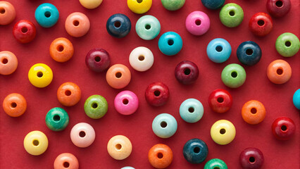 Fototapeta premium Colorful wooden beads scattered randomly on vibrant red background, featuring multiple bright colors including yellow, blue, green, pink, orange, and purple tones.