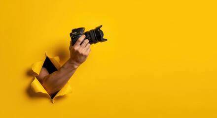 Camera in Hand Breaking Through Yellow Paper Wall Photography Equipment Photo Session Studio Shooting Creative Professional Photographer.