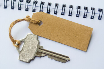 A silver key placed beside a brown cardboard tag on a spiral notebook representing access credentials, password reminder and personal security concept.