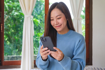 Portrait image of a woman holding and using smart phone on the bed