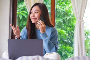 Portrait image of a beautiful woman talking on mobile phone while using laptop computer on the bed