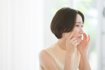 鏡を見ながら顔を触るミドル世代の日本人女性。