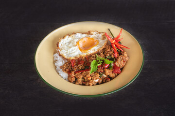 Beautifully presented stir-fried pork with basil and a fried egg, served in a vintage style plate garnished with fresh chilies, cucumber and herbs
