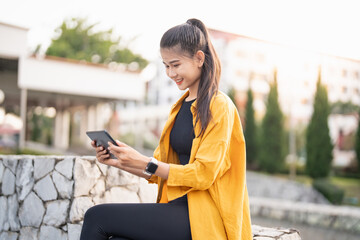 Smiling young Asian woman using digital tablet in urban city